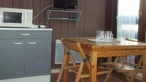 A compact kitchen with a microwave, a flat-screen TV mounted on a wooden shelf, and a dining table with a glass set. - 300m from ski slopes, Ground floor, tv, 21m², Orcières Merlette 1850 (Orcières)