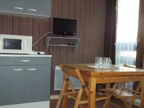 A compact kitchen with a microwave, a flat-screen TV mounted on a wooden shelf, and a dining table with a glass set. - Ground floor, tv, 21m², Orcières Merlette 1850 (Orcières)