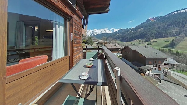 A wooden balcony with a table and chairs, overlooking a mountainous landscape. - 1st floor, balcony, tv, ski locker, 77m², Le Grand Bornand (Le Grand-Bornand)