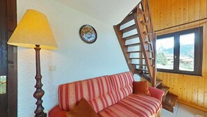 A cozy room with a wooden staircase, a striped sofa, a lamp, and a decorative plate on the wall. - 1st floor, balcony, tv, ski locker, 77m², Le Grand Bornand (Le Grand-Bornand)