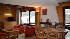 A cozy living room with wooden walls, a fireplace, a dining table with chairs, and a television on a wooden cabinet. - 1st floor, balcony, tv, ski locker, 77m², Le Grand Bornand (Le Grand-Bornand)