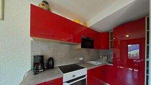 A compact kitchen with red cabinets, a white stove, and a coffee maker. - 1st floor, balcony, tv, ski locker, 77m², Le Grand Bornand (Le Grand-Bornand)