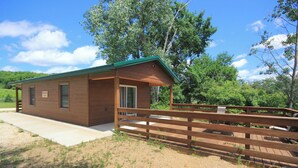A small, single-story wooden cabin with a green roof, a porch, and a fenced yard. - Quaint Lakeview Cabin  (Wadena)