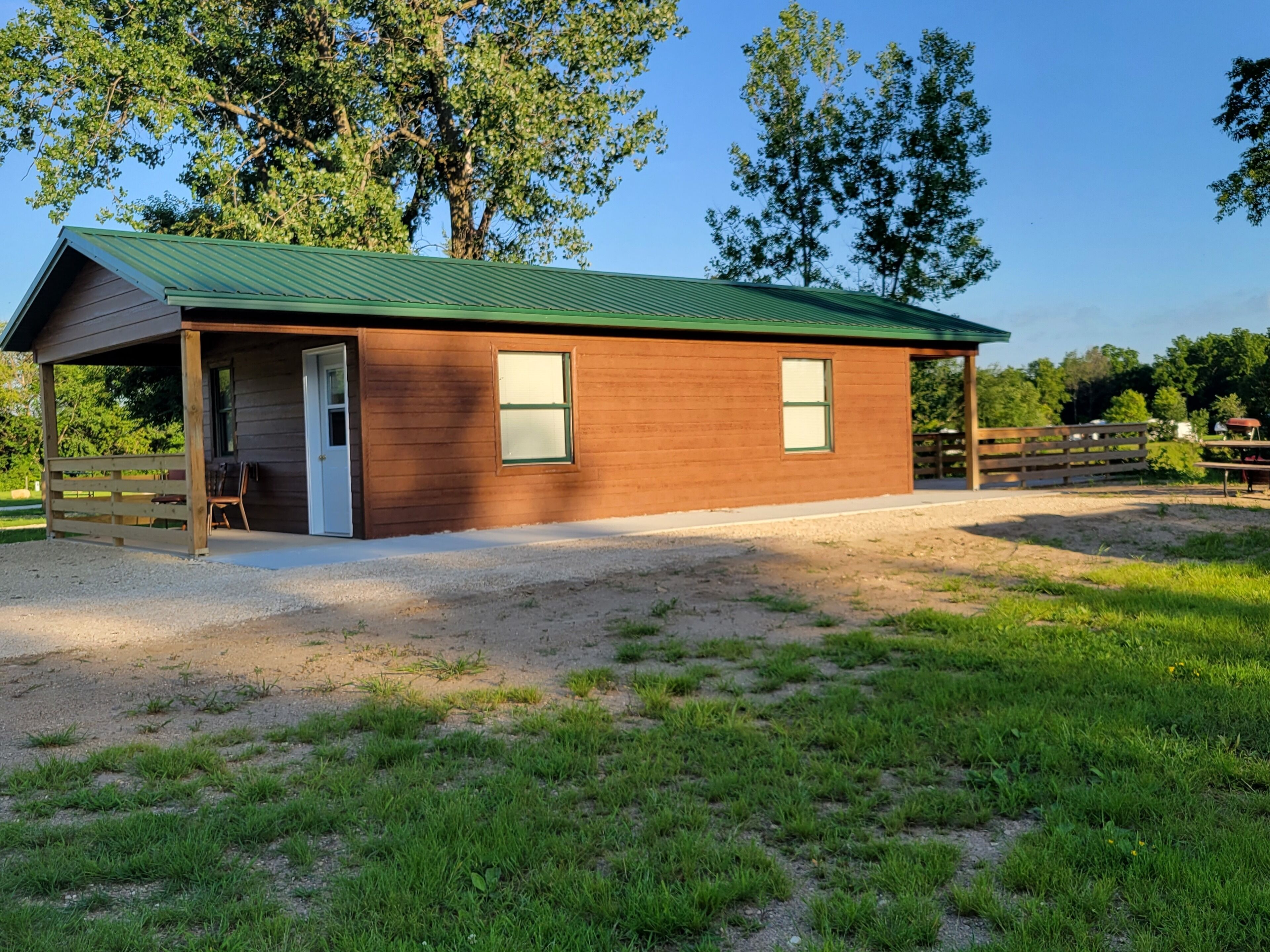 A wooden building with a green roof, a covered entrance, and a fenced area.