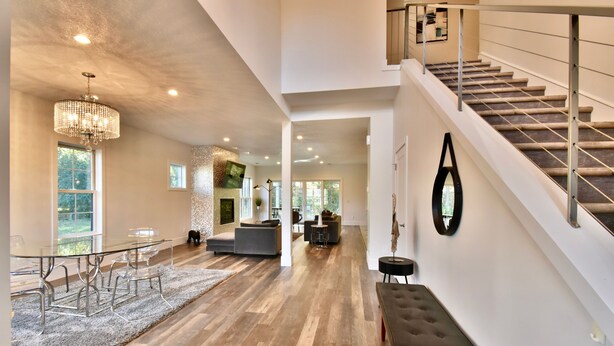 Un vaste espace de vie comprenant un coin repas avec une table en verre, un escalier et une vue sur l’extérieur.