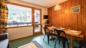 A dining area with a wooden table set for four, a television on the wall, and a view of a snowy landscape through large windows. - 1st floor, view mountain, balcony, ski locker, 34m², Valmorel (Valmorel)
