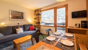 A cozy living room with a sofa, a dining table set for four, and a large window with a view of buildings. - 1st floor, view mountain, balcony, ski locker, 34m², Valmorel (Valmorel)