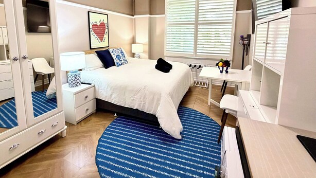 A hotel room with a bed, bedside tables, a desk, a chair, a wardrobe, and a window with blinds. - Brisbane CBD Studio: Modern Comfort Great Location (Brisbane City)