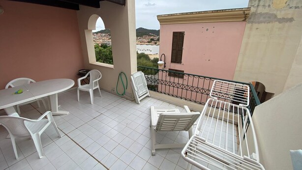 Un balcon avec une table et des chaises, un tuyau d’arrosage et une vue sur la ville.