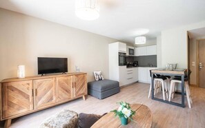 Een modern appartement met een houten kast, een flatscreen-tv, een grijze bank, een eettafel met stoelen en een keukenhoek.