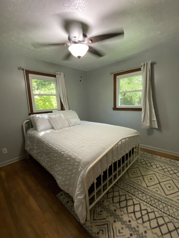 A bedroom with a bed, a ceiling fan, two windows with curtains, and a patterned rug. - 225 The Creek - Peaceful & Cozy (Andrews)