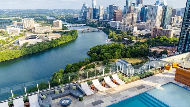 Un espace piscine aménagé sur le toit, avec des chaises longues et une vue sur les toits de la ville et le fleuve.