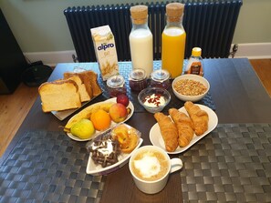 A breakfast table with toast, fruits, croissants, a coffee cup, and various condiments.