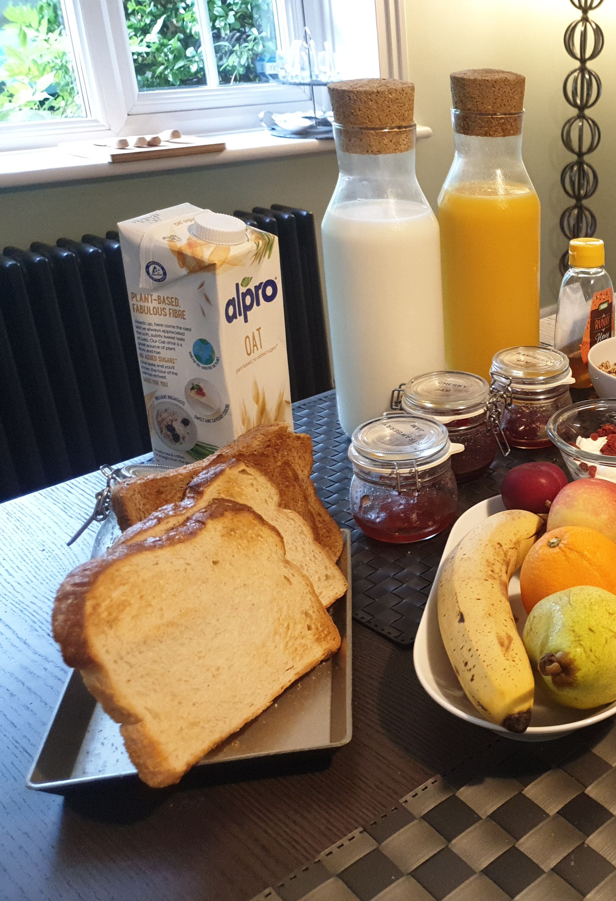 Aamiaispöydällä on kauramaitoa, appelsiinimehua, hilloa ja hedelmiä.