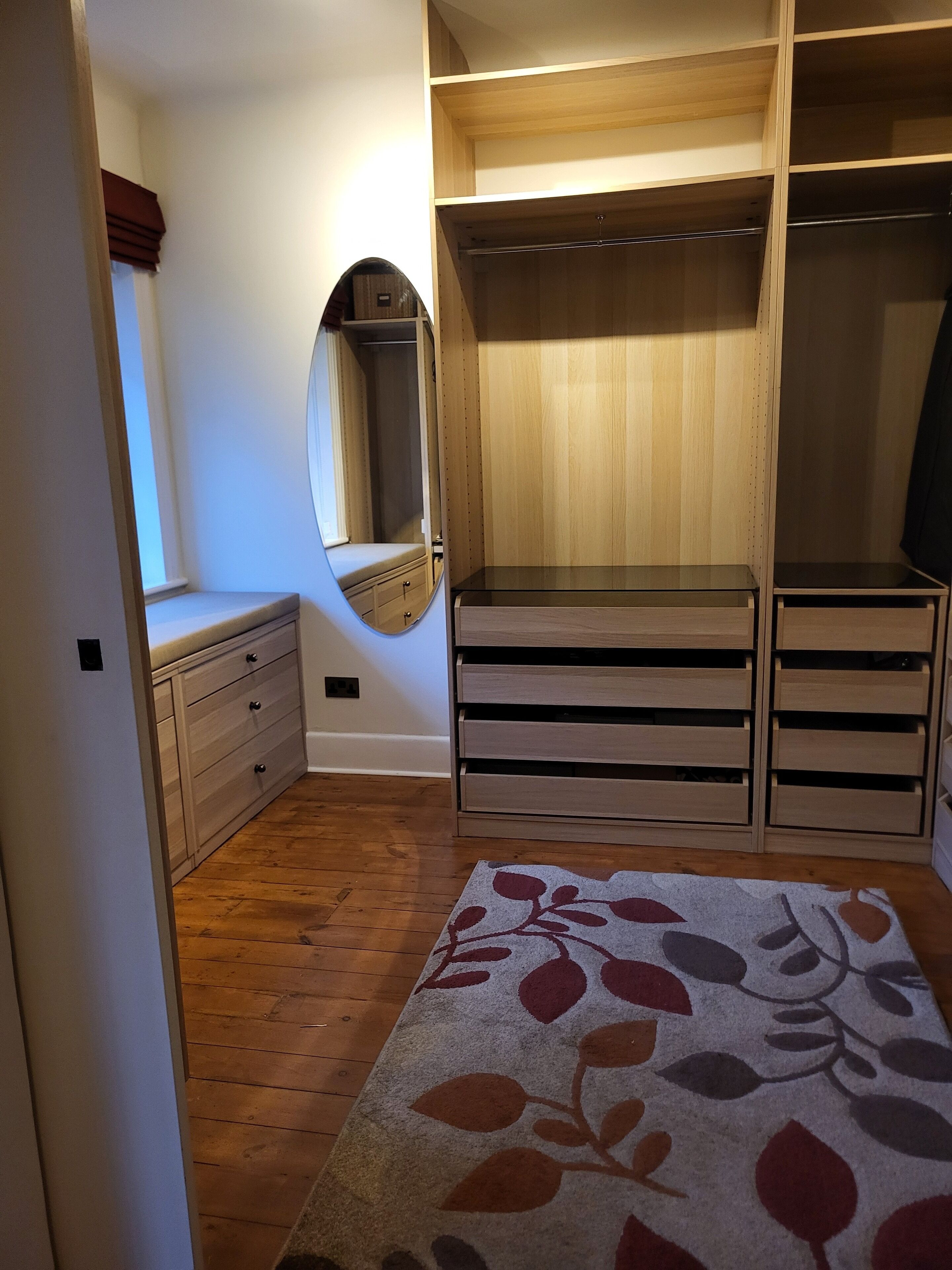 A walk-in closet with wooden shelving, a mirror, and a bench.
