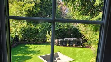 A view through a window of a well-maintained garden with a central lawn area, surrounded by dense foliage and trees.