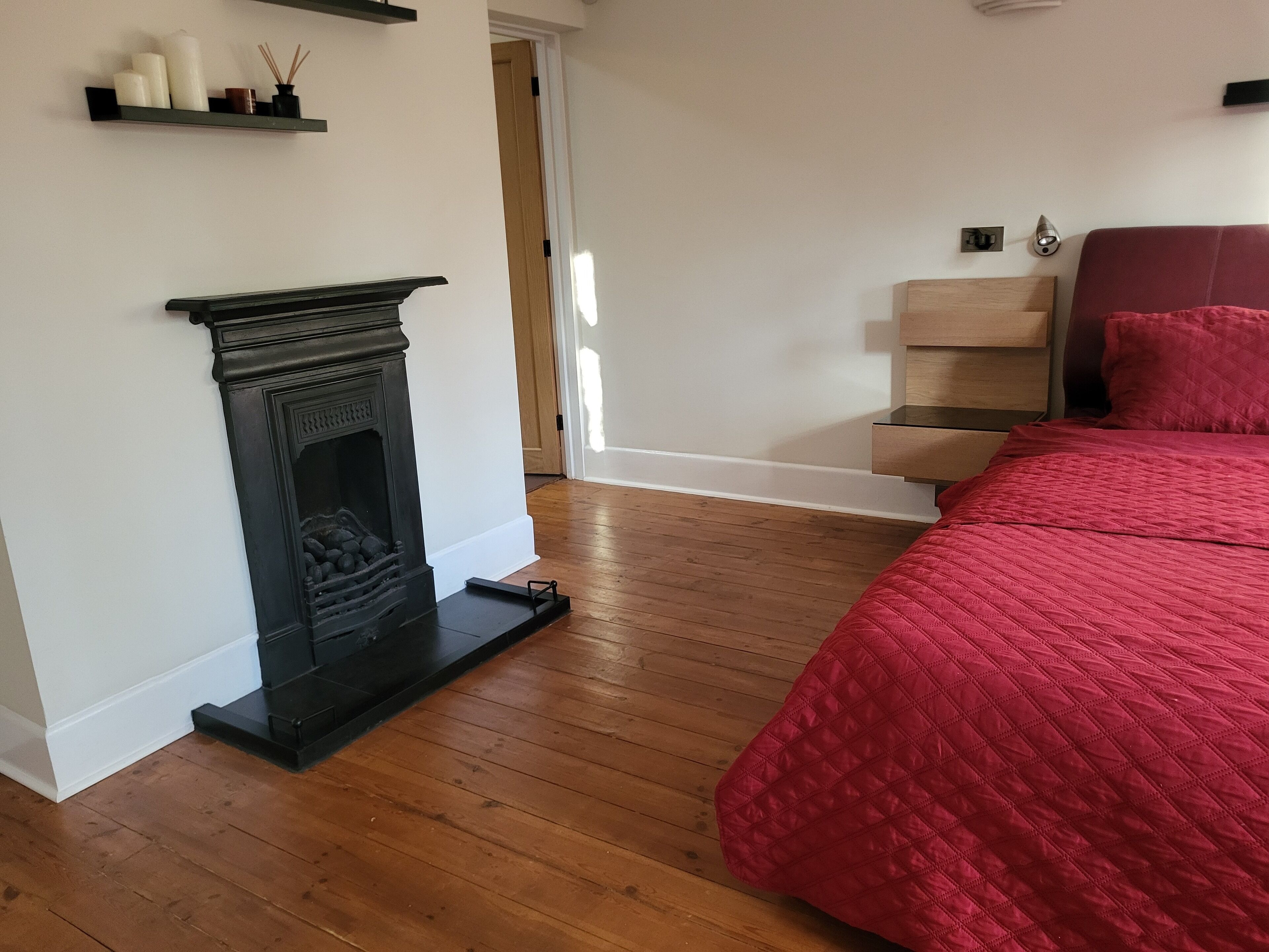 Een slaapkamer met een open haard, een rode bed en houten vloeren.