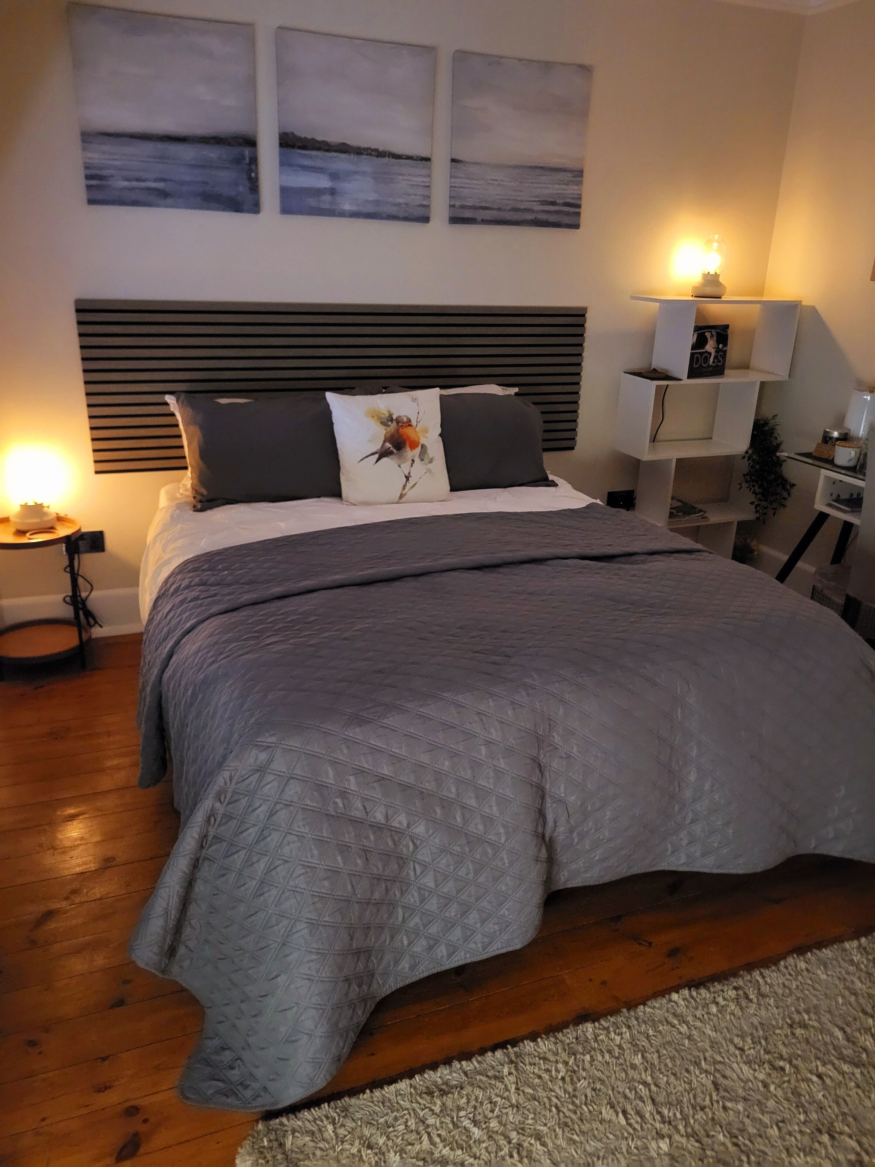 Quarto com cama, mesa de cabeceira, luminária e decoração na parede.