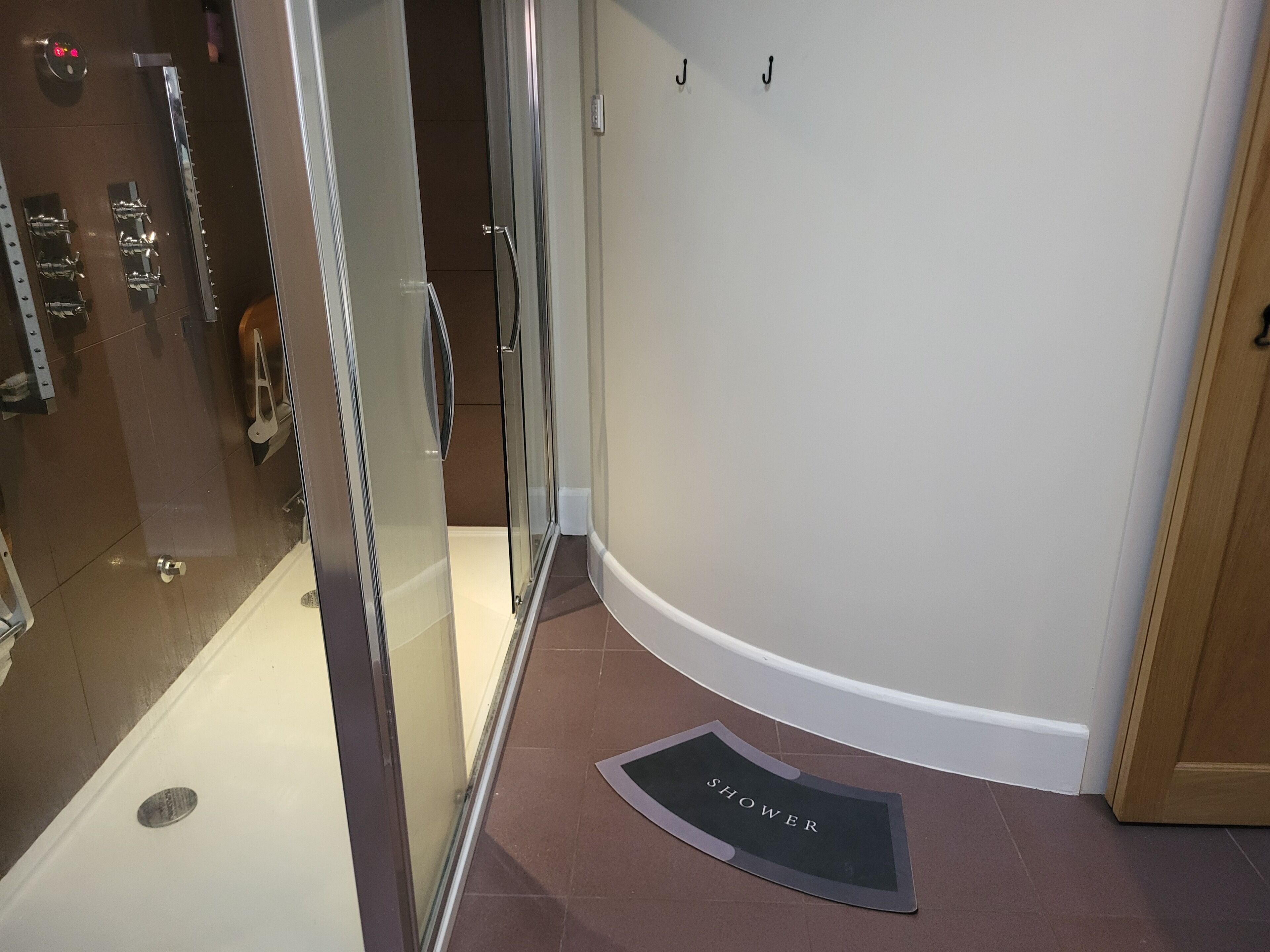 A shower area with glass doors, a shower mat labeled "SHOWER", and a towel rack with hooks.