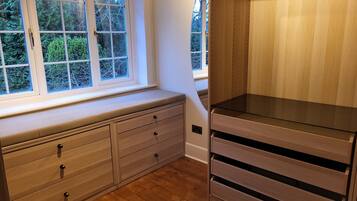 A room with a built-in bench along a window, wooden flooring, and a built-in cabinet with drawers.