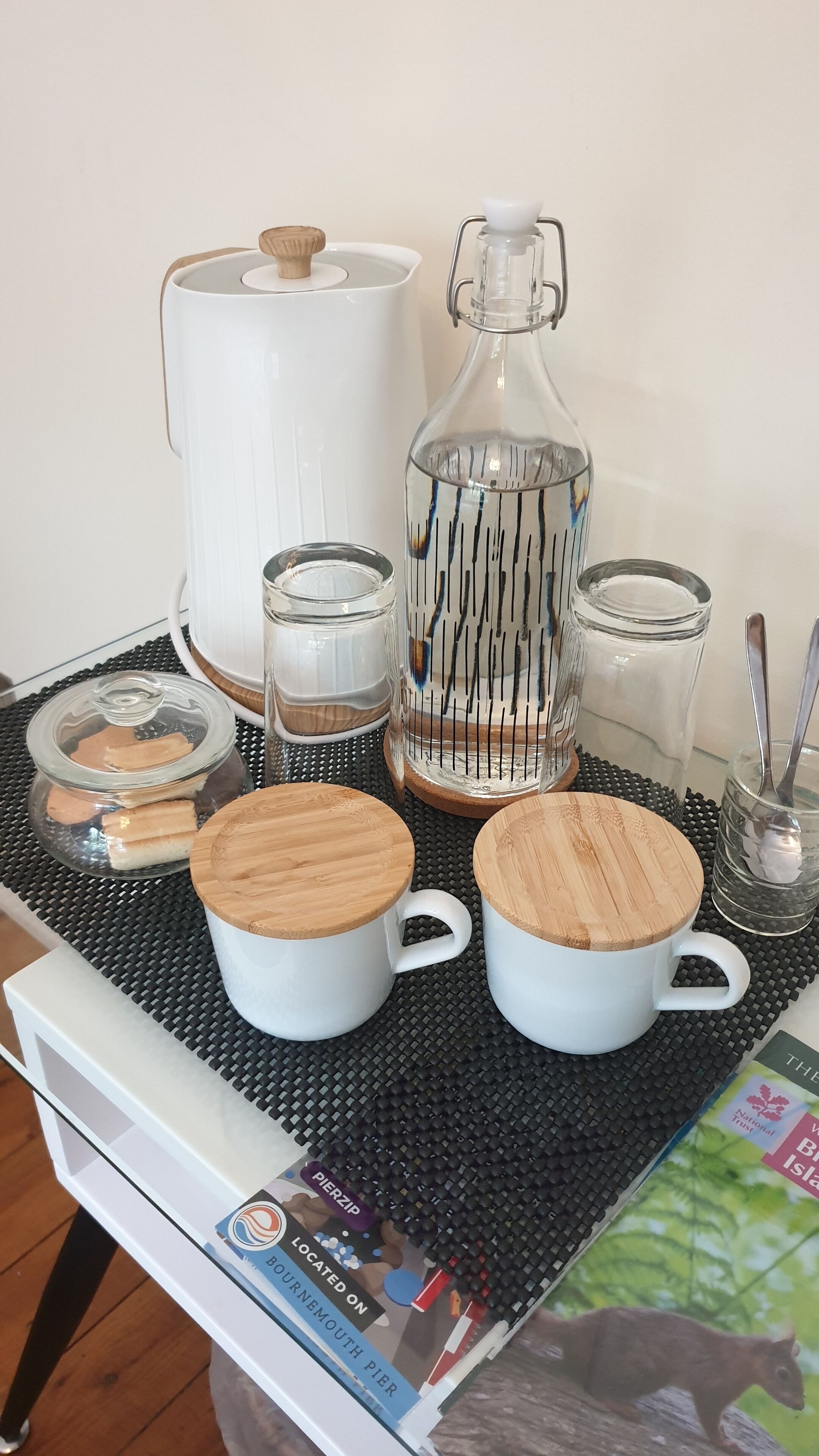 Una mesa con diferentes vasos, incluyendo una jarra, copas y un frasco, junto con dos tazas con tapas de madera.