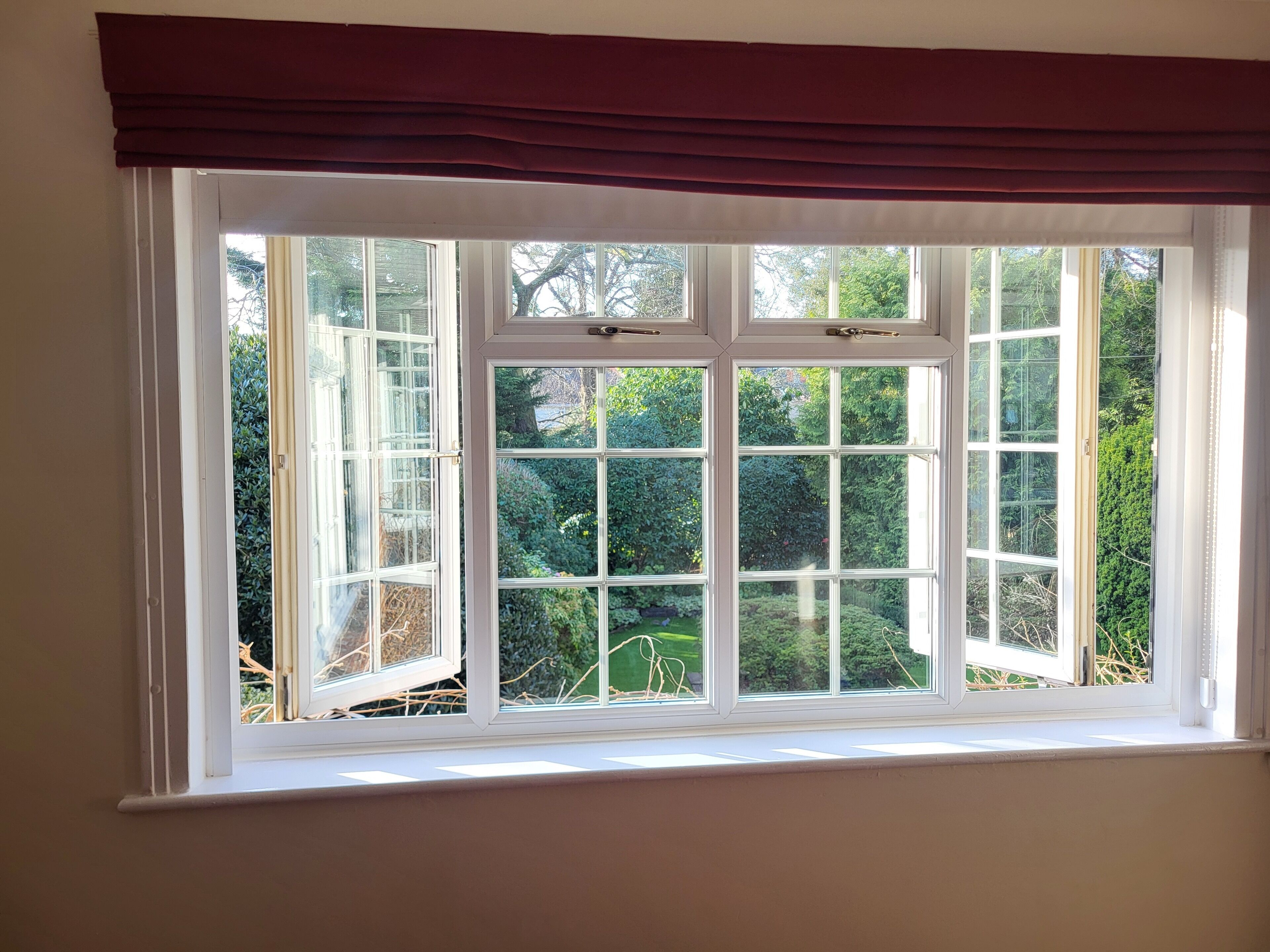 A window with a white frame and a dark brown valance, offering a view of a lush garden.