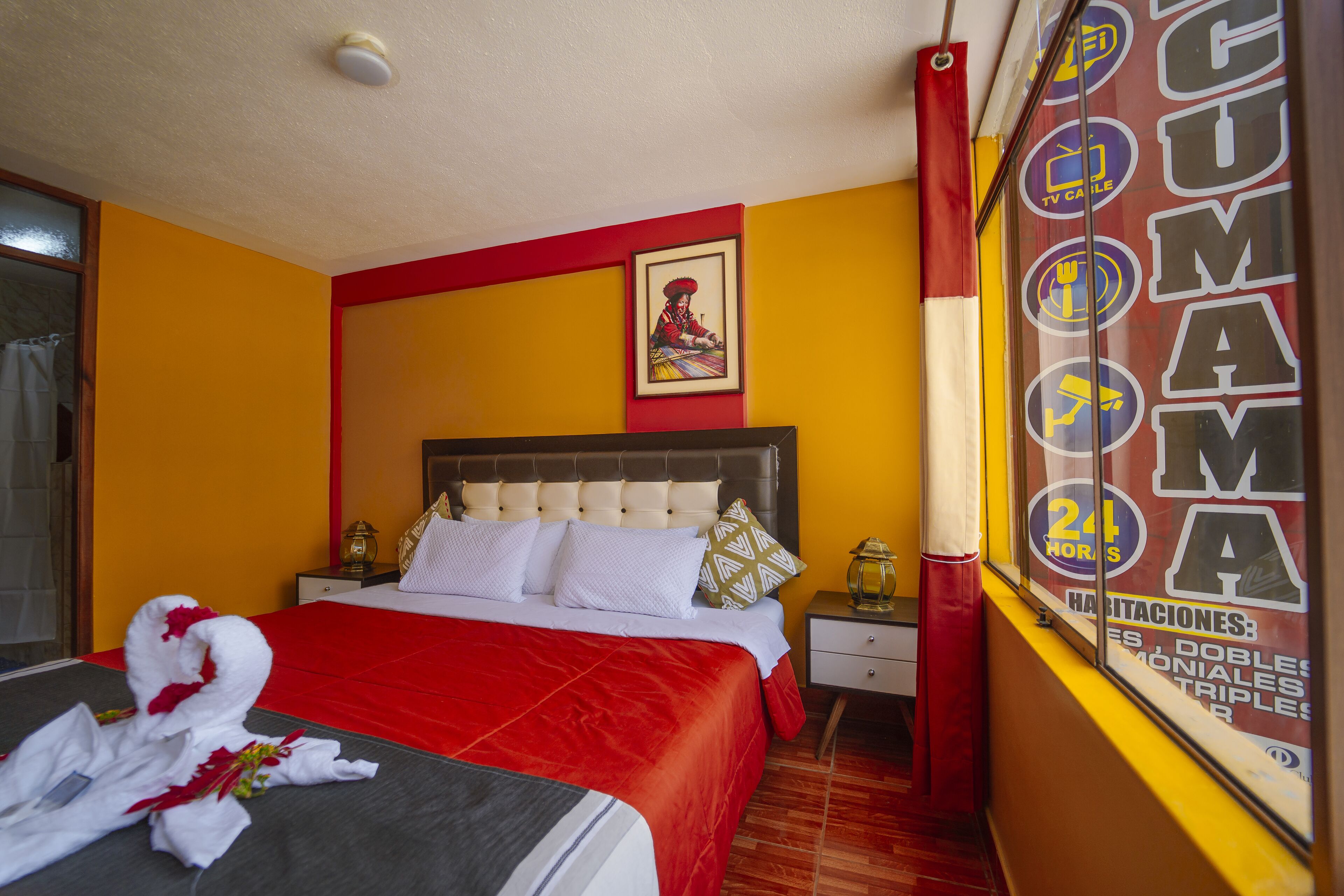 A hotel room with a red bedspread, a neatly made bed with white linens, a framed picture on the wall, and a window with a sign advertising 24-hour service.