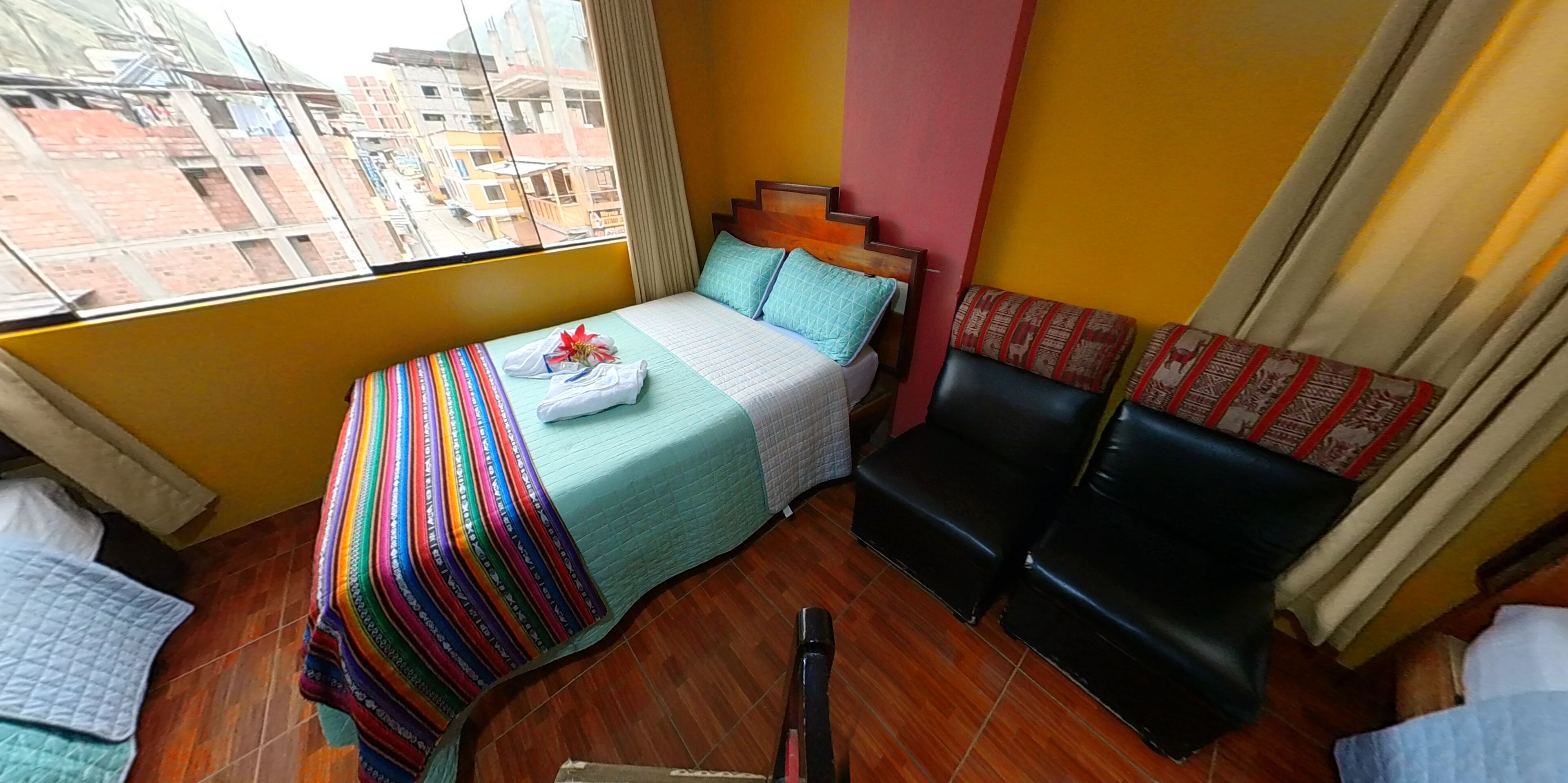 A small, compact hotel room with a bed, a small seating area, and a window offering a city view.