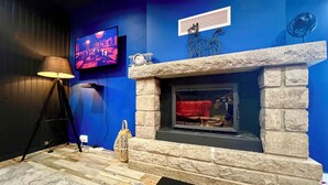 A room with a stone fireplace, a television mounted on the wall, and a lamp. - LoveRoom by Gîtes d'Armor (Plelo)