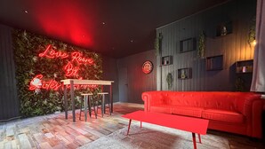 A modern living room with a red sofa, a red coffee table, and a neon sign reading "Love Room By Gites." - LoveRoom by Gîtes d'Armor (Plelo)