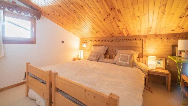 Una habitación acogedora de madera con una cama, una ventana y una mesita de noche con una lámpara.