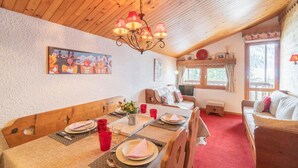 Un comedor acogedor con techo de madera, una araña y una mesa de comedor dispuesta con platos, vasos y un jarrón de flores.