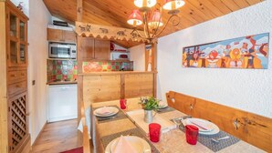 Un comedor con una mesa de madera dispuesta para cuatro personas, una araña y un cuadro en la pared.