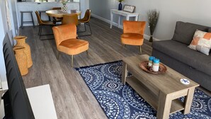 Ein modernes Wohnzimmer mit einer Couch, zwei orangefarbenen Sesseln, einem Holztisch und einem gemusterten Teppich.