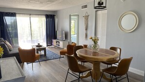 Ein modernes Wohnzimmer mit einem runden Holzesstisch, umgeben von braunen Stühlen, einer Couch und einem Fernseher auf einem weißen Schrank.