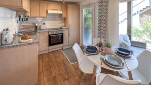 Une cuisine moderne avec des meubles en bois, un four encastré et un coin repas avec des chaises blanches et des assiettes bleues.