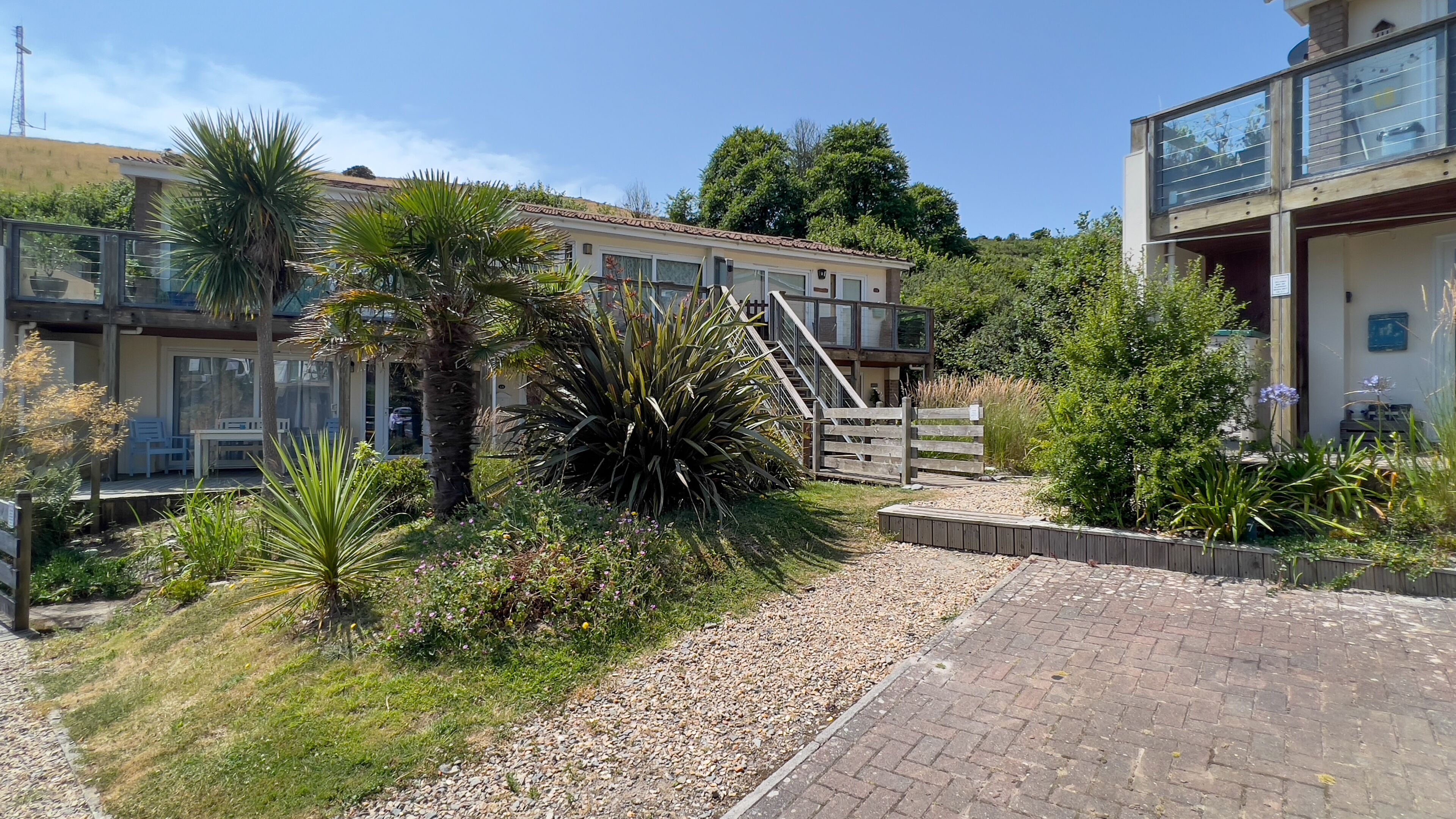 A residential building with a covered outdoor area, a gravel path, and various plants.