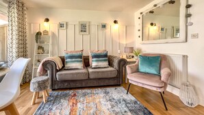 Un salon avec un canapé gris, un fauteuil rose et un tapis à motifs.