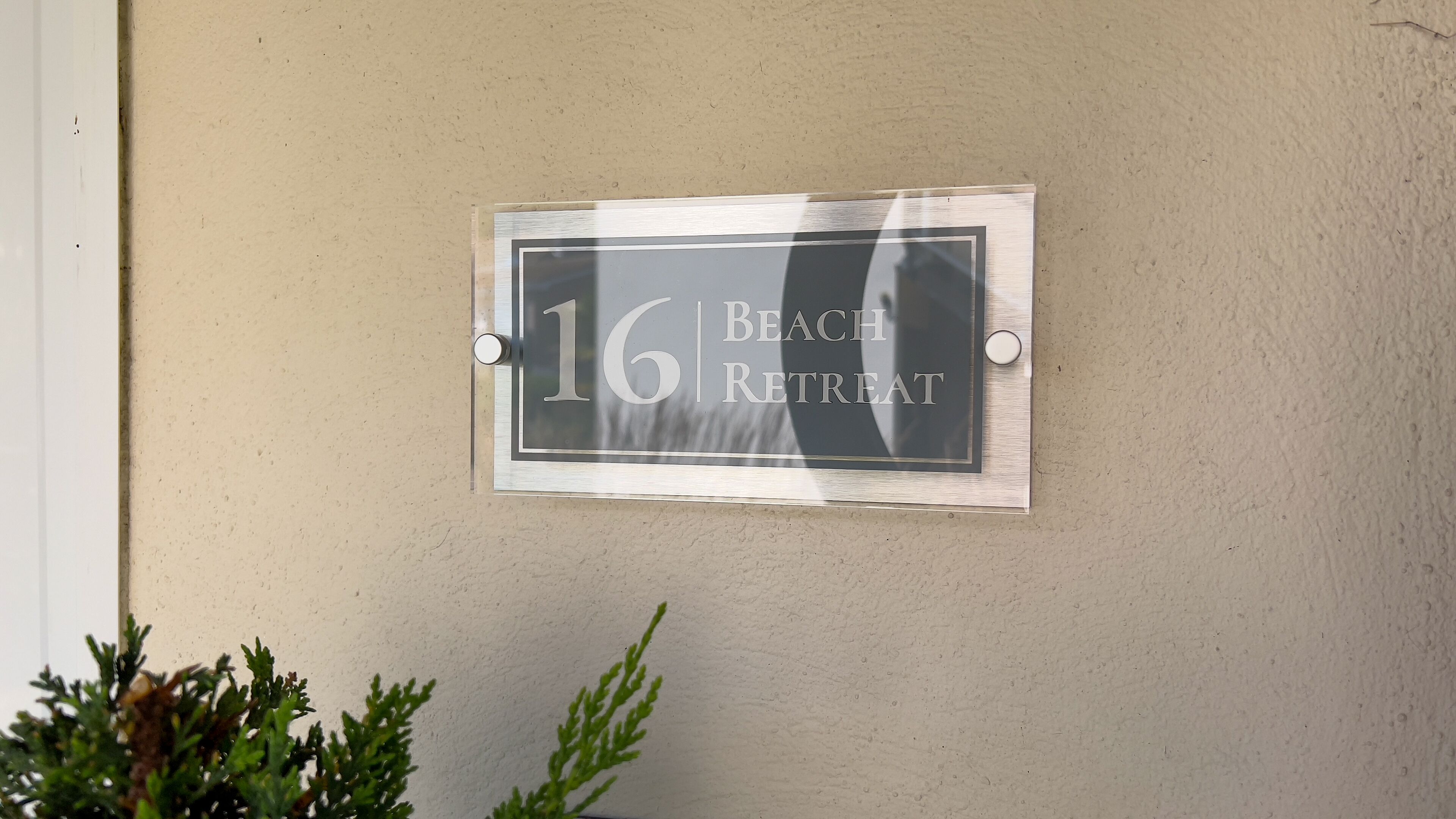 A house number sign for "16 Beach Retreat" mounted on a wall.