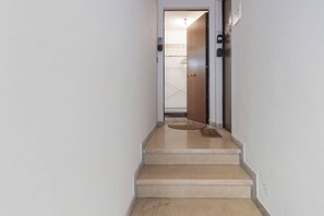 Um corredor estreito com escada carpetada dando para uma porta.