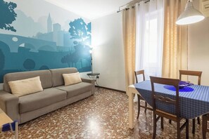 A living room with a sofa, a dining table with chairs, a wall mural, and a floor with a patterned tile design.