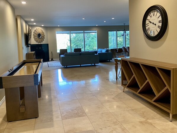 A spacious living room with a large clock, a pool table, and a blue sofa. - Emerald on Jewel Lake (Anchorage)