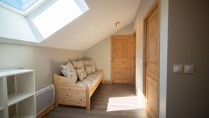 A loft bedroom with a skylight, wooden floor, a sofa with floral cushions, and a wooden door. - 380m from shops, 4th floor, view mountain, balcony, parking, ski locker, 85m², Valmorel (Les Avanchers-Valmorel)