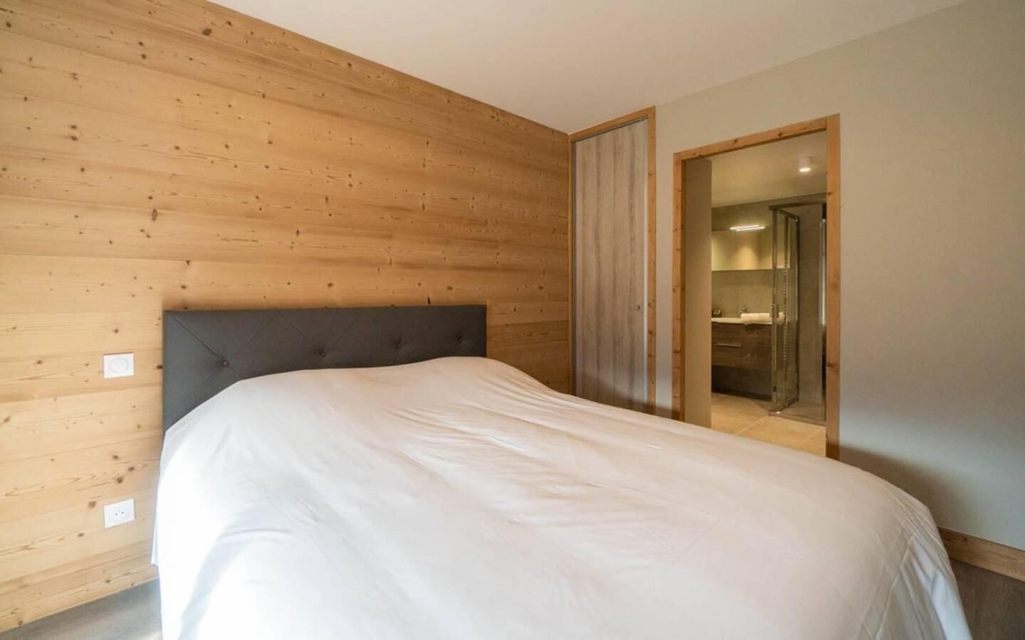 A bedroom with a wooden headboard, a large bed, and a bathroom visible through an open door.