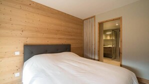 A bedroom with a wooden headboard, a large bed, and a bathroom visible through an open door. - 380m from shops, 4th floor, view mountain, balcony, parking, ski locker, 85m², Valmorel (Les Avanchers-Valmorel)