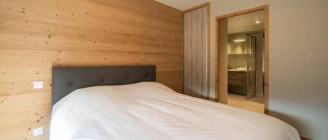 A bedroom with a wooden headboard, a large bed, and a bathroom visible through an open door.