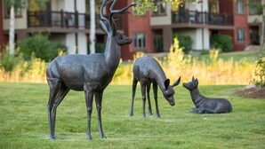 Une sculpture de cerf se trouve dans une zone herbeuse, avec un bâtiment en arrière-plan.