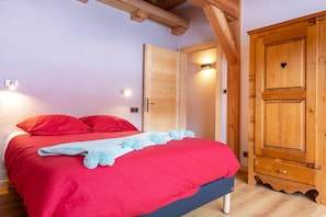 A bedroom with a red bed, a wooden wardrobe, and a door with a heart-shaped cutout.