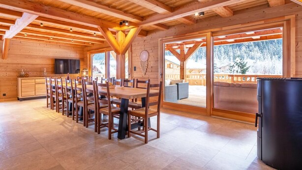 L’intérieur d’un chalet en bois comprend un coin repas, de grandes fenêtres et une vue sur un paysage enneigé.
