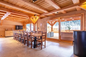 A wooden cabin interior with a dining area, large windows, and a view of a snowy landscape.
